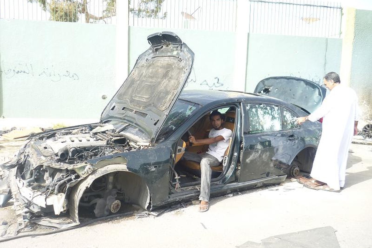 Naveed sitting in the wreckage of a burnt out car in Tripoli